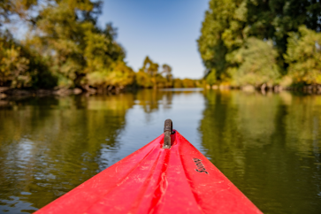 Die Spitze eines roten Kanus zeigt in Flussrichtung. Im Hintergrund wird das Fussurfer gezeigt.