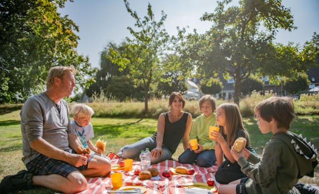 Eine glückliche Familie sitzt bei sonnigem Wetter auf einer Wiese und macht ein Picknick
